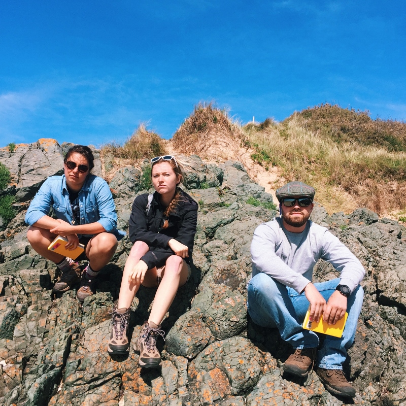 3 students giving their best Peaky Blinders looks while sitting on an outcrop