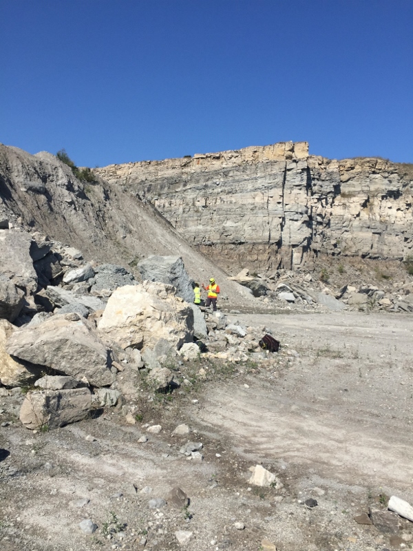 student examines a rock pile with a quarry highwall in the background