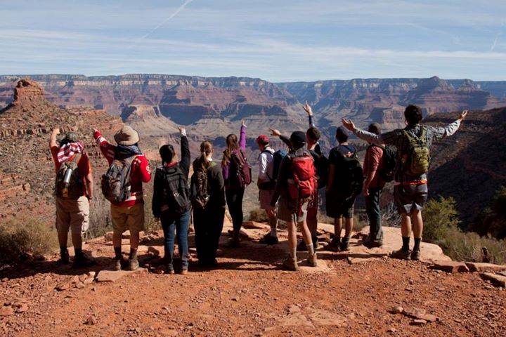 students with arms raised looking across the rim of the Grand Canyon