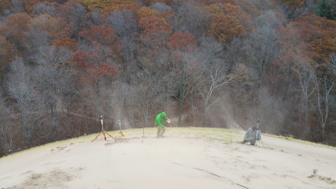 sand swirling around researchers on a dune slope high above the surrounding forest