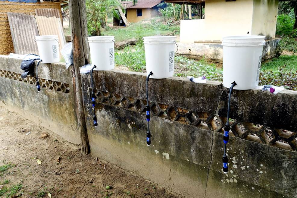 buckets draining into water filters sitting on a low wall in a village