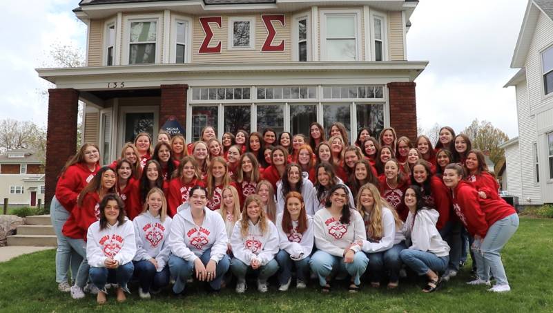 Members of the Sigma Sigma sorority smiling in front of their on-campus house